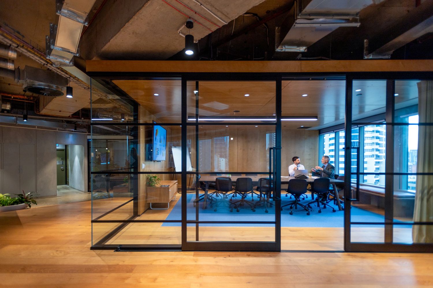 Two men having a discussion inside a modern glass-walled conference room.