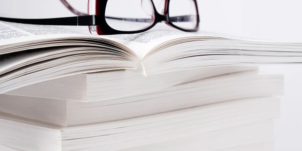 Stack of books with an open book and glasses on top.