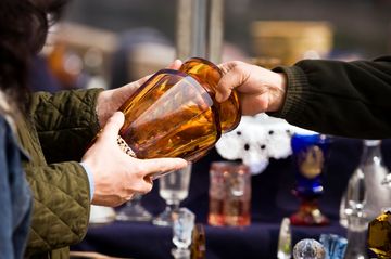 Two people exchanging an amber glass vase.