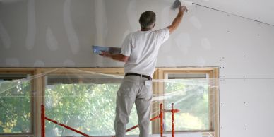 Man plastering drywall in room under renovation.