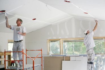 Two men painting a ceiling white.