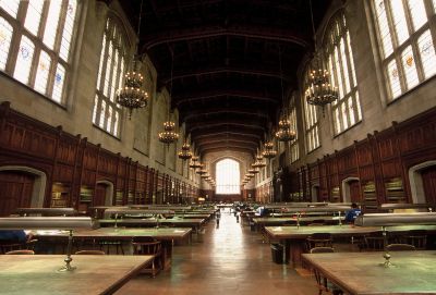 A grand, historic library reading room with wooden tables and large windows.