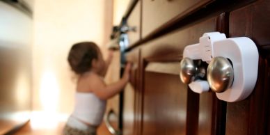 Childproof cabinet lock with toddler in background.