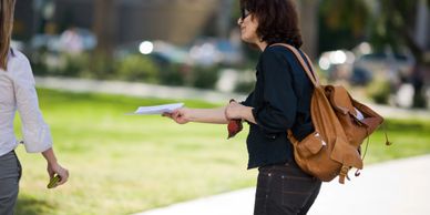 Woman handing out flyers on a sunny sidewalk.