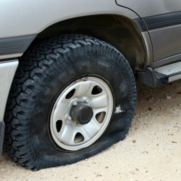Close-up of a flat tire on a vehicle parked on a dirt surface.