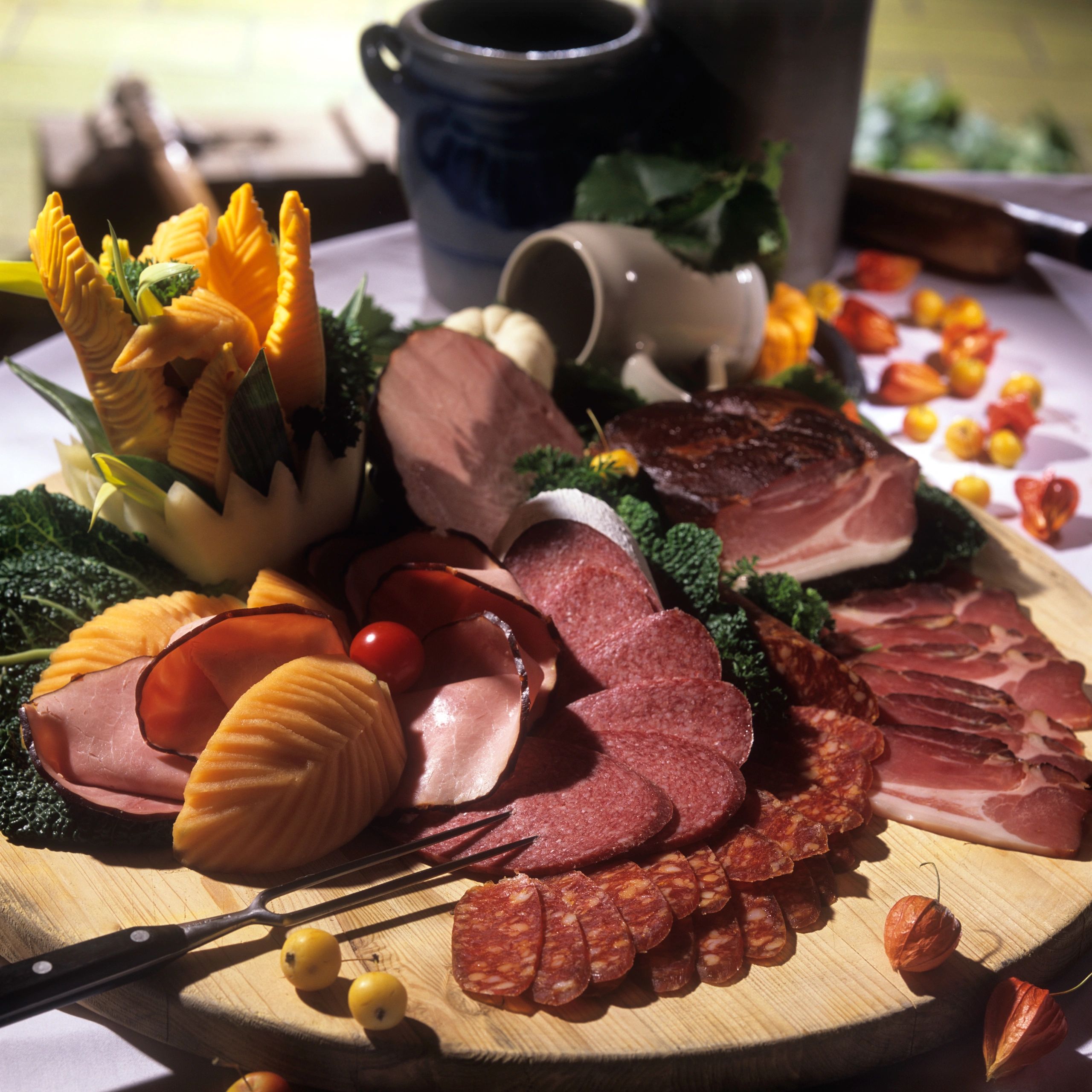 A wooden platter with assorted sliced meats and decorative carved vegetables.
