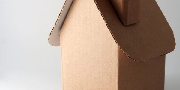 Close-up of a small cardboard house model with a chimney on a plain background.