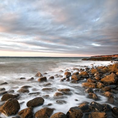 Rocky shoreline under a cloudy sky with waves washing over stones.