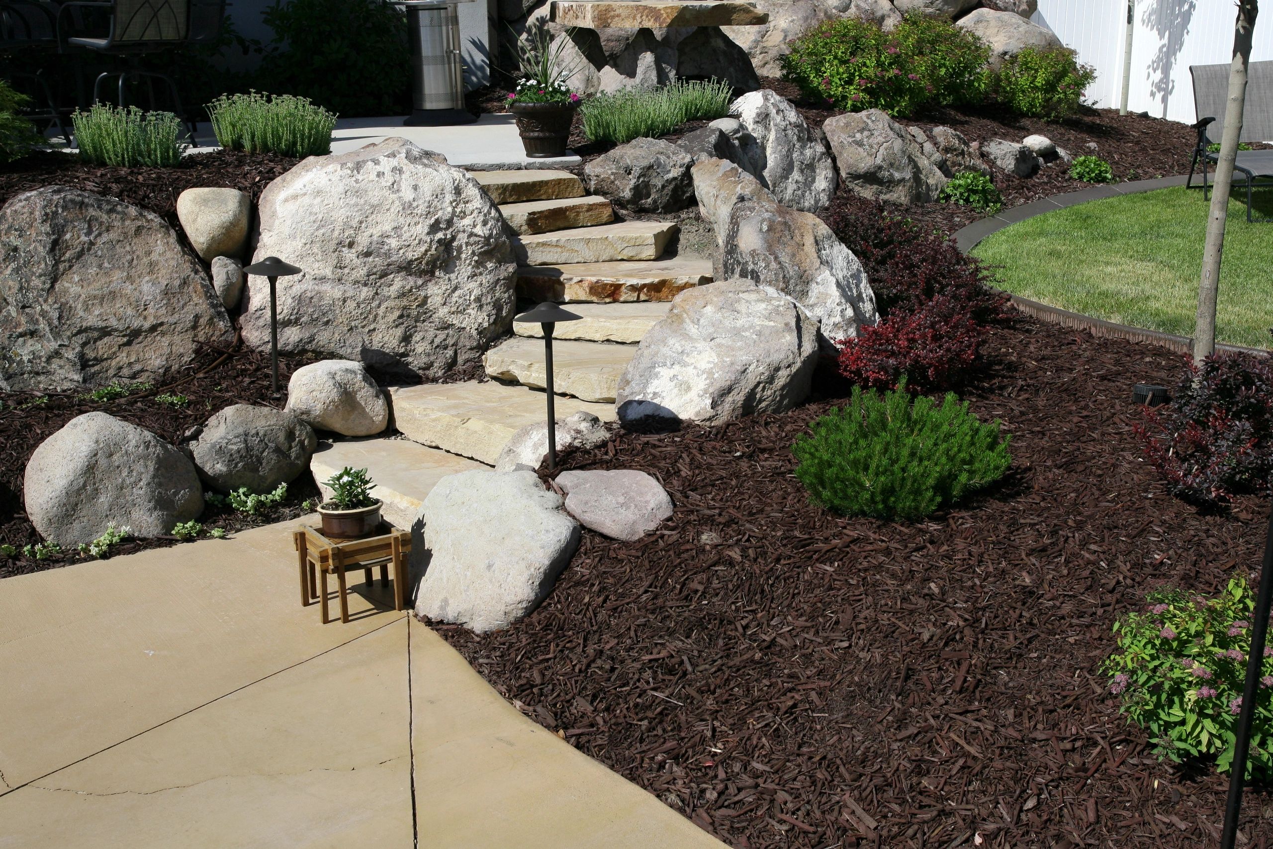 Curved stone wall with potted plants and outdoor seating behind it.