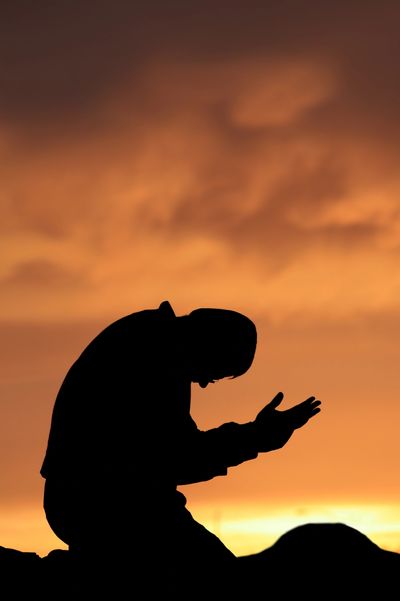 Silhouette of a person praying at sunset.