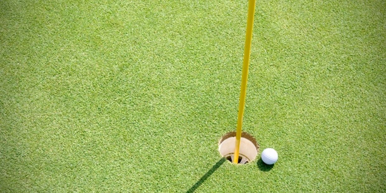 Golf ball near the hole on a green putting surface.