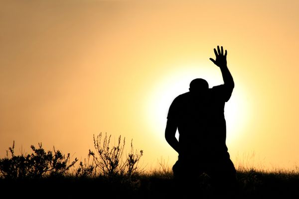 Silhouette of a person raising one hand at sunset.