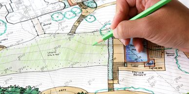 Hand coloring a detailed landscape design plan with a green pencil.