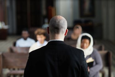 A man in a suit speaking to a small group in a church.