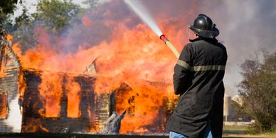 Firefighter extinguishing a large house fire with a water hose.