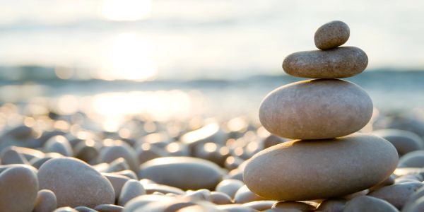 A stack of smooth stones balanced on a pebble-covered beach at sunset.