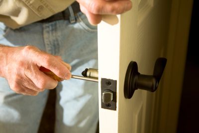 A person is installing or repairing a door handle with a screwdriver.