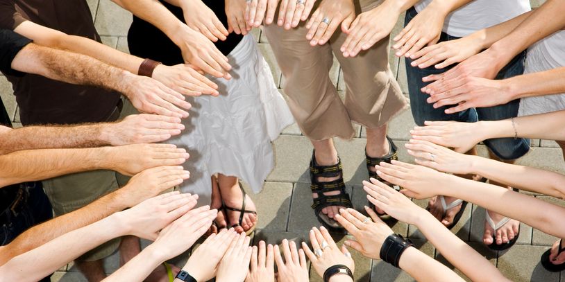 Group of people standing in a circle with hands extended inward.