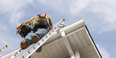 A worker climbs a ladder to repair a house gutter.