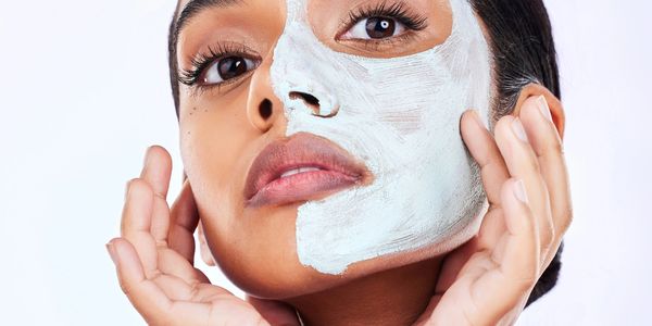 Woman applying a white facial mask on half of her face.
