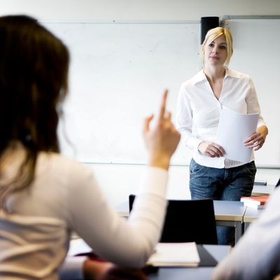 Student raising hand to ask question while teacher listens attentively in classroom.