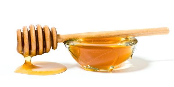 Honey dipper with honey dripping beside a bowl of honey.