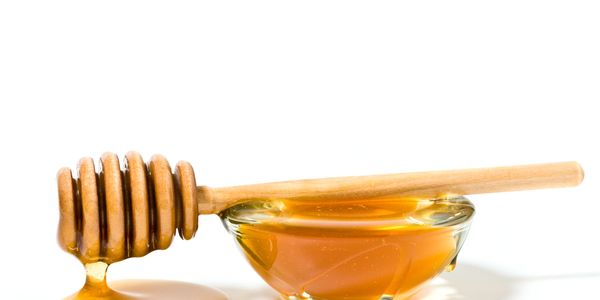 Honey dipper with honey dripping beside a bowl of honey.