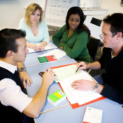 Four adults engaged in a discussion around a table with books and documents.