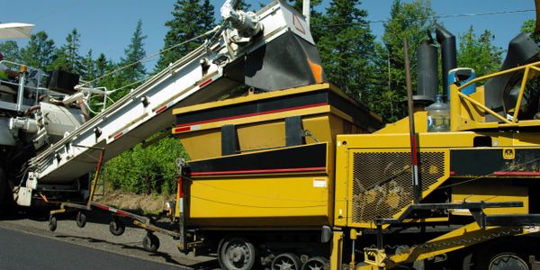 Yellow asphalt paving machine laying new road surface outdoors.