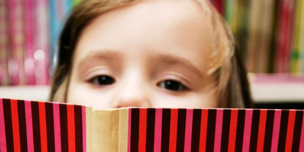 A child peeks over a striped book cover in a colorful library.