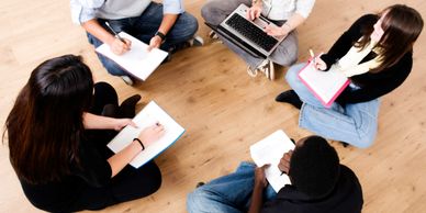 Group of five students sitting on the floor studying and discussing.