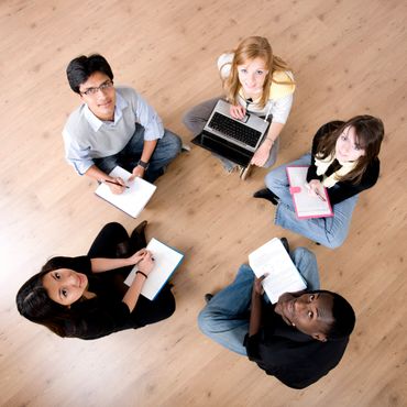 Five diverse students sitting in a circle on the floor studying together.