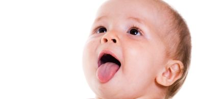 Baby sticking out tongue against white background.