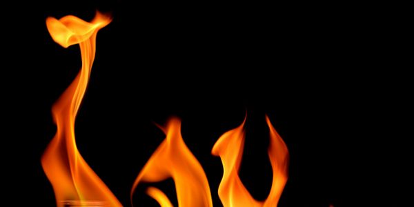 Stacks of coins burning with flames against a black background.