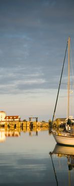 Sailboat docked in a calm harbor during sunset with golden reflections.