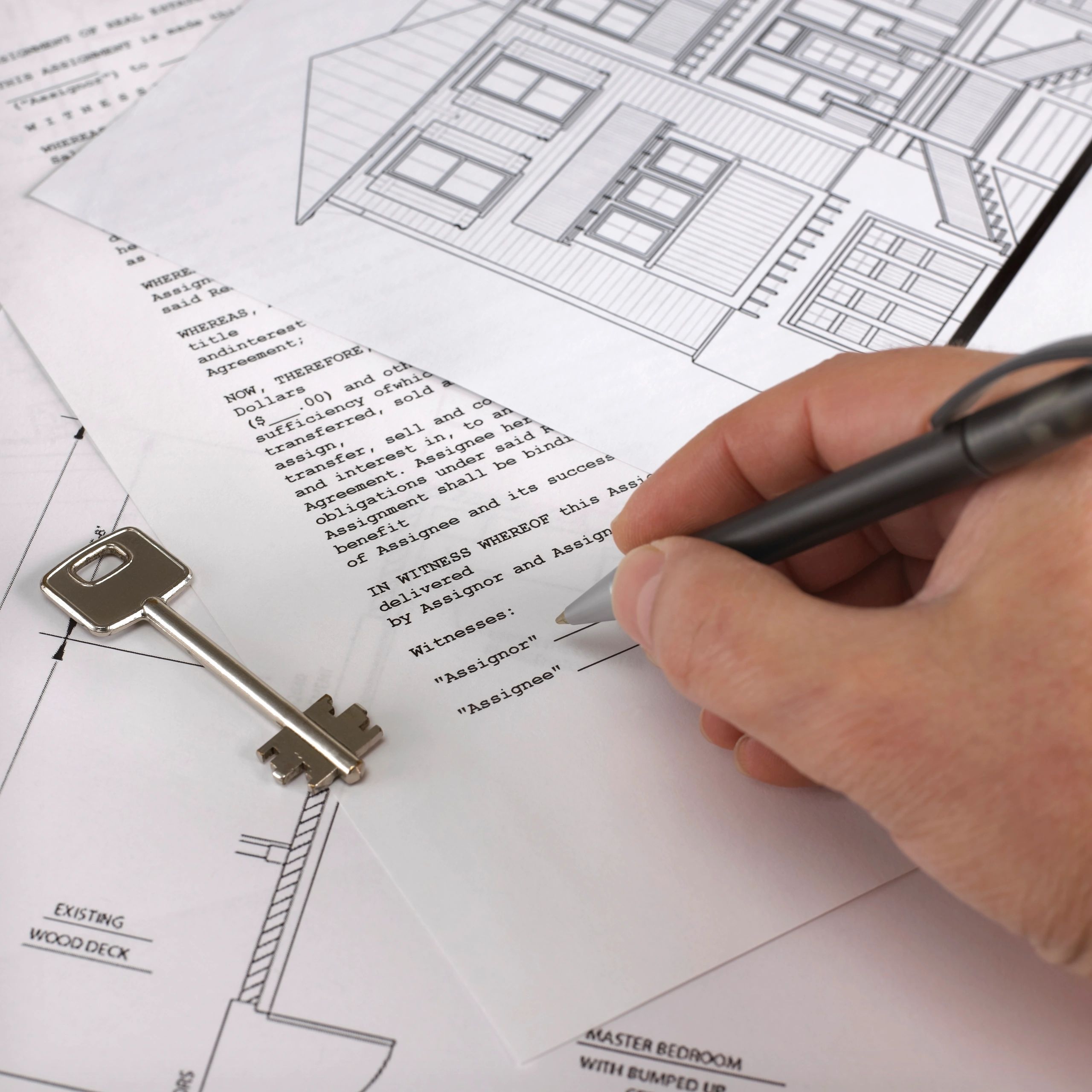 Hand signing a real estate agreement with house plans and a key.