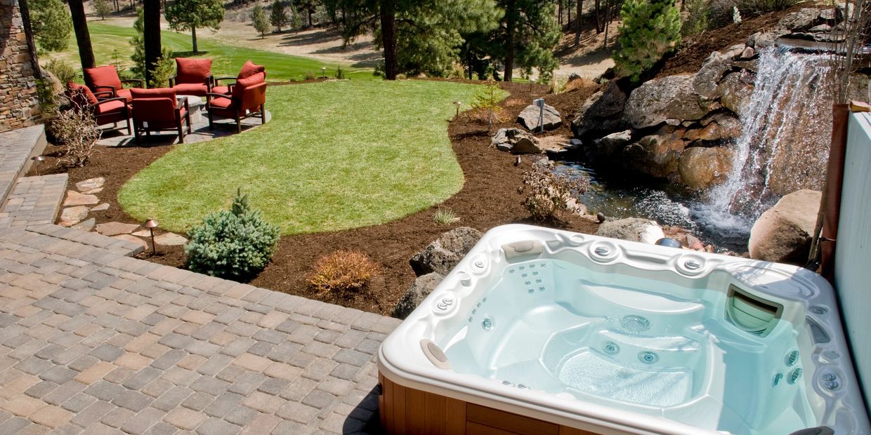Outdoor patio with hot tub and seating area surrounded by nature.