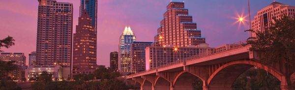 City skyline with a bridge at twilight reflecting on water.