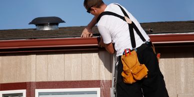 A man on a ladder fixing the roof gutter on a sunny day.