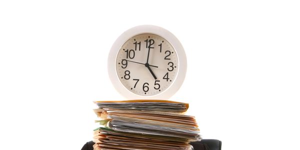 Clock showing 5:00 above a large stack of documents.