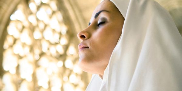 A woman in a white hijab with closed eyes, bathed in soft light.