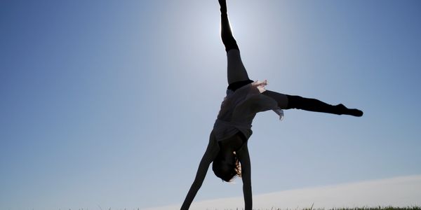 Person doing a cartwheel outdoors against a clear sky.
