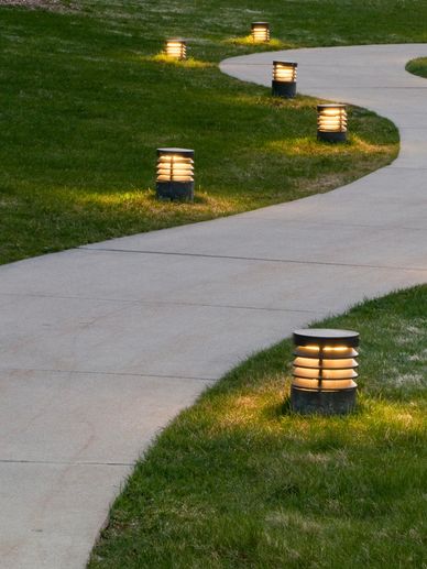 Curved pathway illuminated by small ground lights through a grassy area at dusk.