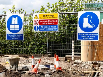 Construction site with safety signs for clothing and footwear requirements.