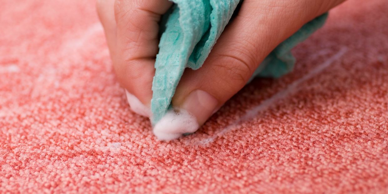 Hand cleaning a red carpet with foam and a cloth.