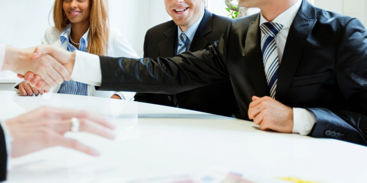 Business people shaking hands across a white table.