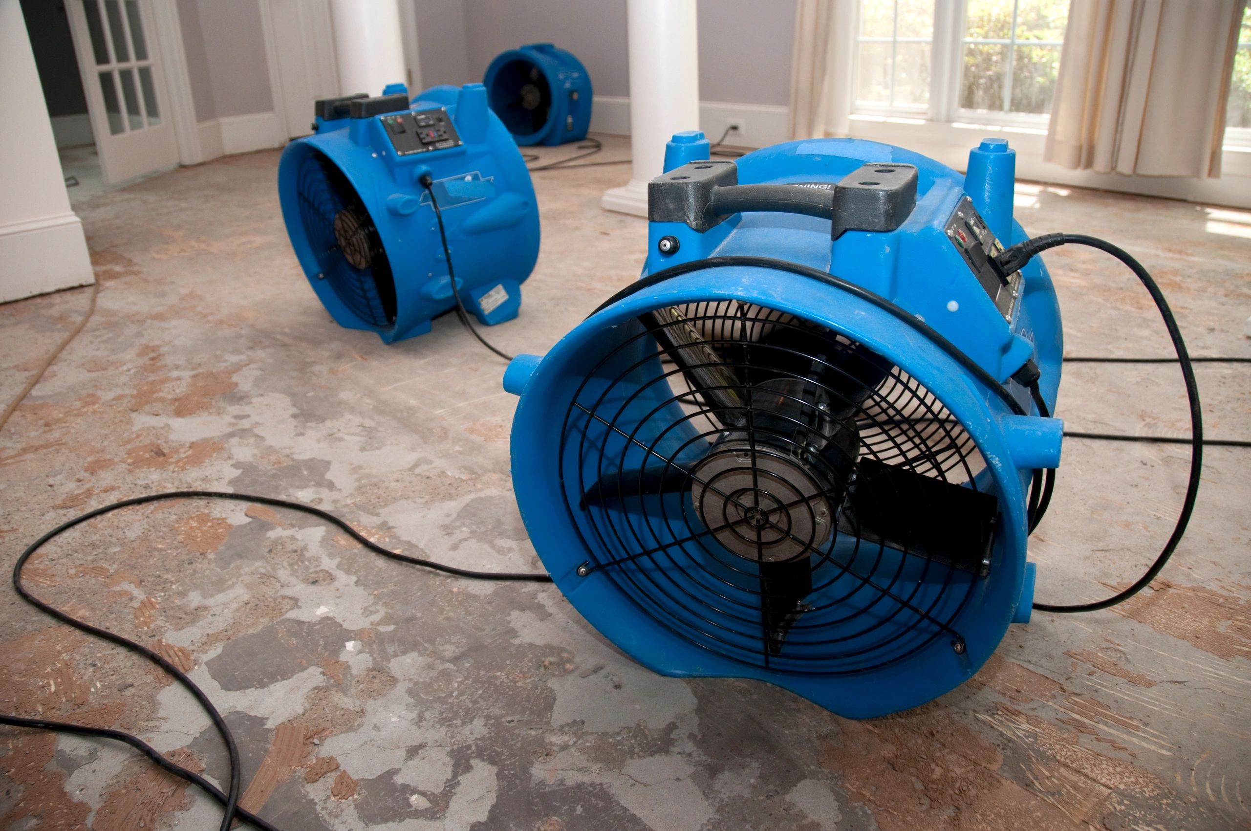 Blue industrial fans drying a damaged floor inside a house.