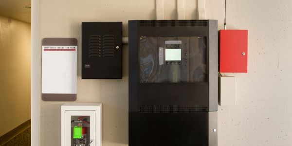 Wall-mounted fire safety and alarm control panels with emergency evacuation plan.