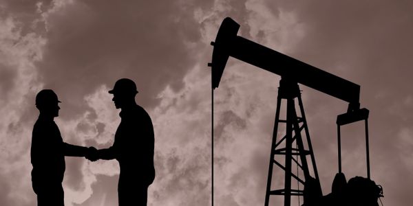 Two workers shaking hands near an oil pumpjack at sunset.