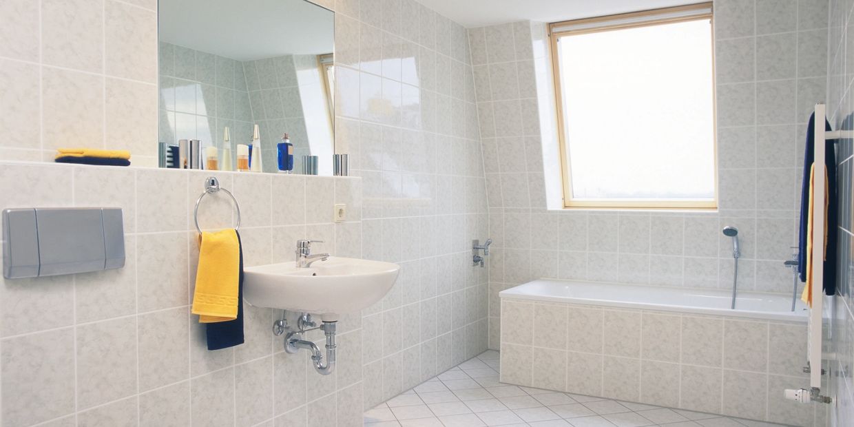 Bright, clean bathroom with white tiles, a bathtub, and yellow towels.